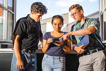Drei Studierende schauen gemeinsam auf einen Tablet